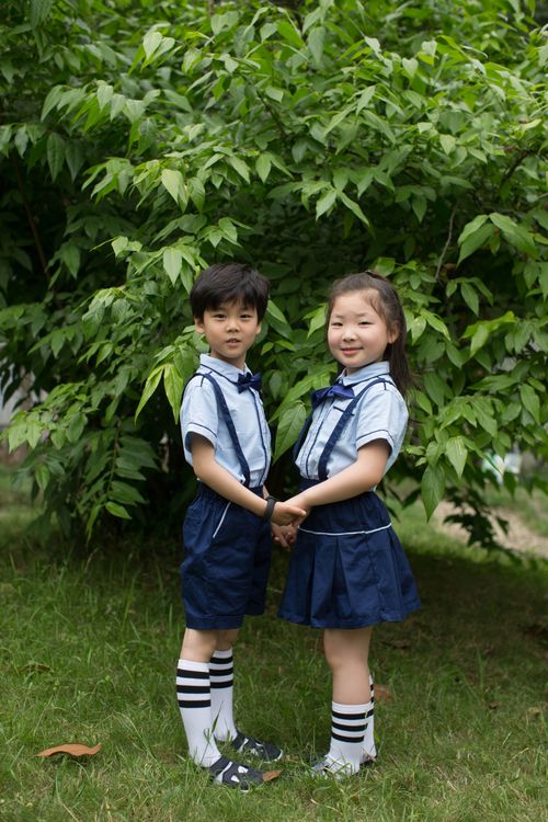 Free Two children in school uniforms stand holding hands in front of greenery outdoors. Stock Photo