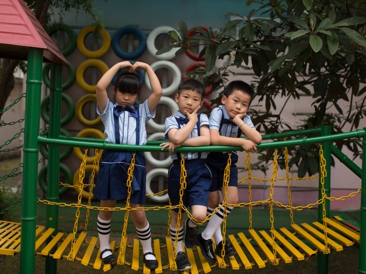 Three children in uniform having fun on a vibrant playground bridge outdoors.