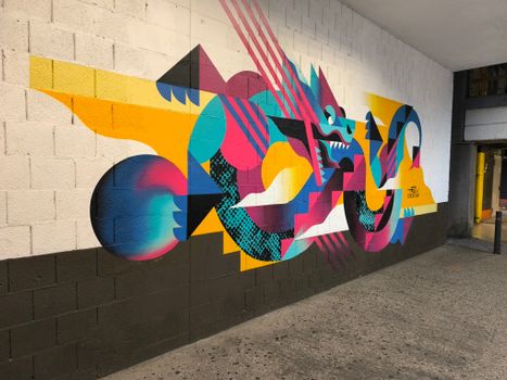 Colorful dragon mural with geometric patterns on a city wall, showcasing vibrant street art.