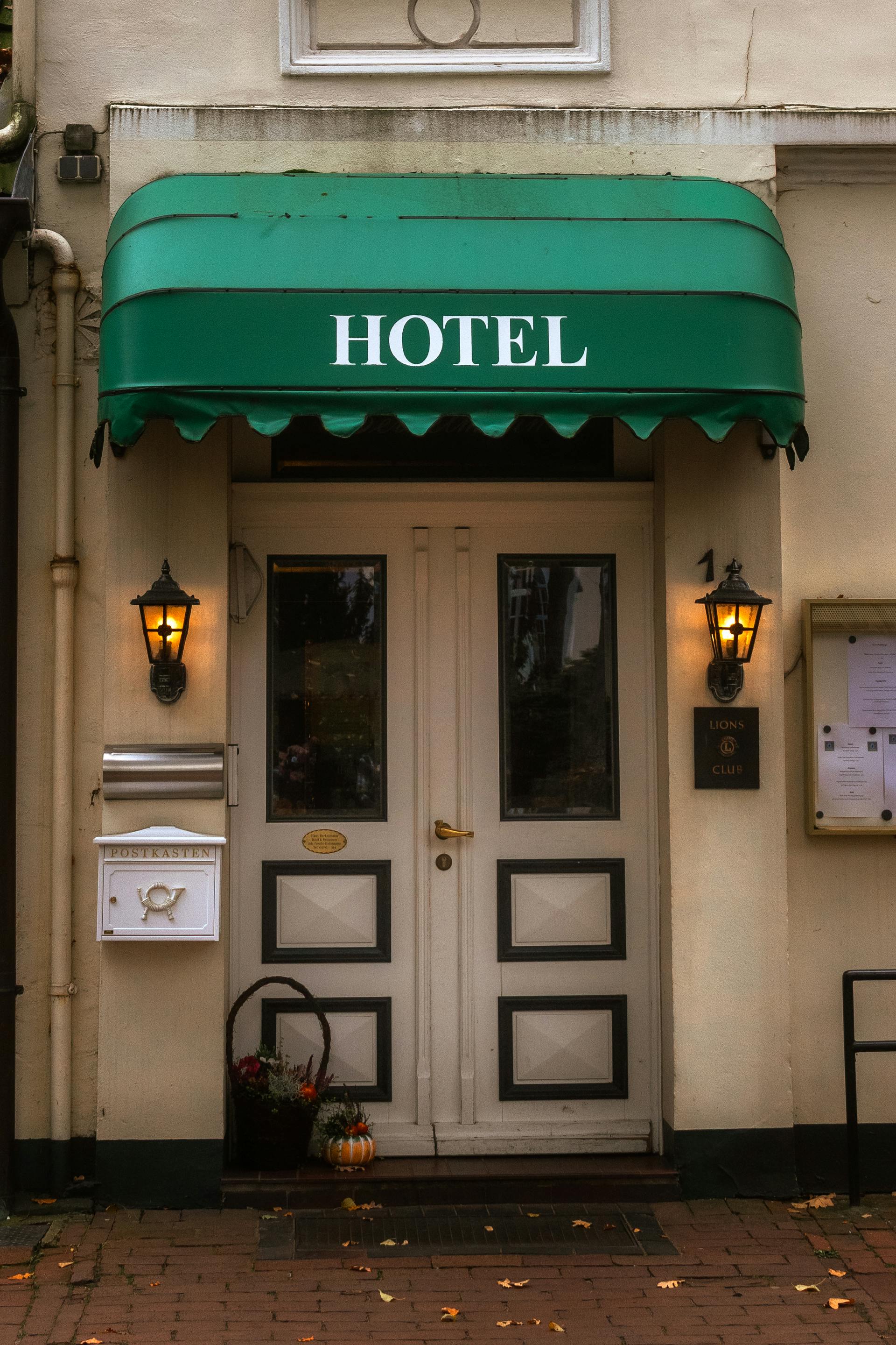 Cozy hotel entrance with a green awning and warm lanterns, inviting ambiance.