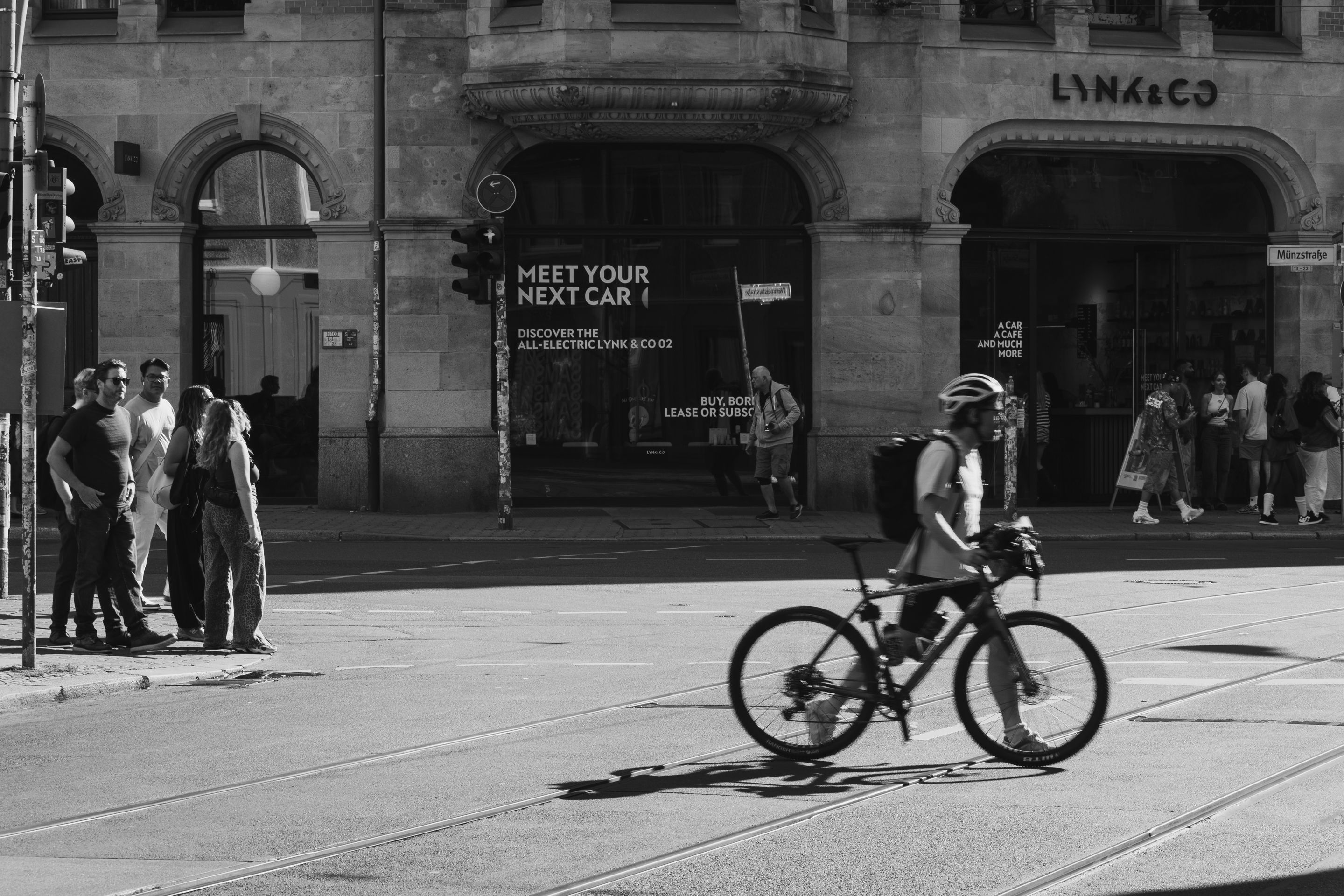 Black and white photo of a cyclist and pedestrians at a Berlin intersection.