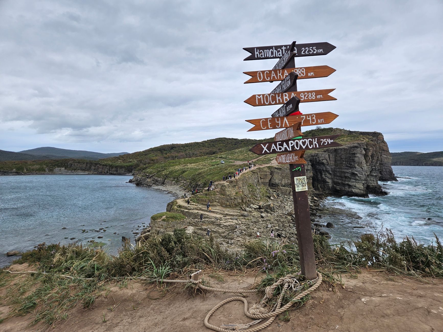 Scenic view of a coastal cliff with a directional signpost pointing to various cities.