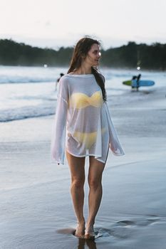 A woman in a bikini and cover-up enjoys a sunset stroll on Phuket's beach.