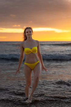 Woman in yellow bikini walking on a beach at sunset in Phuket, Thailand.