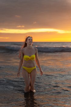 Woman in yellow bikini walks in ocean at Phuket, Thailand during sunset, embracing nature.