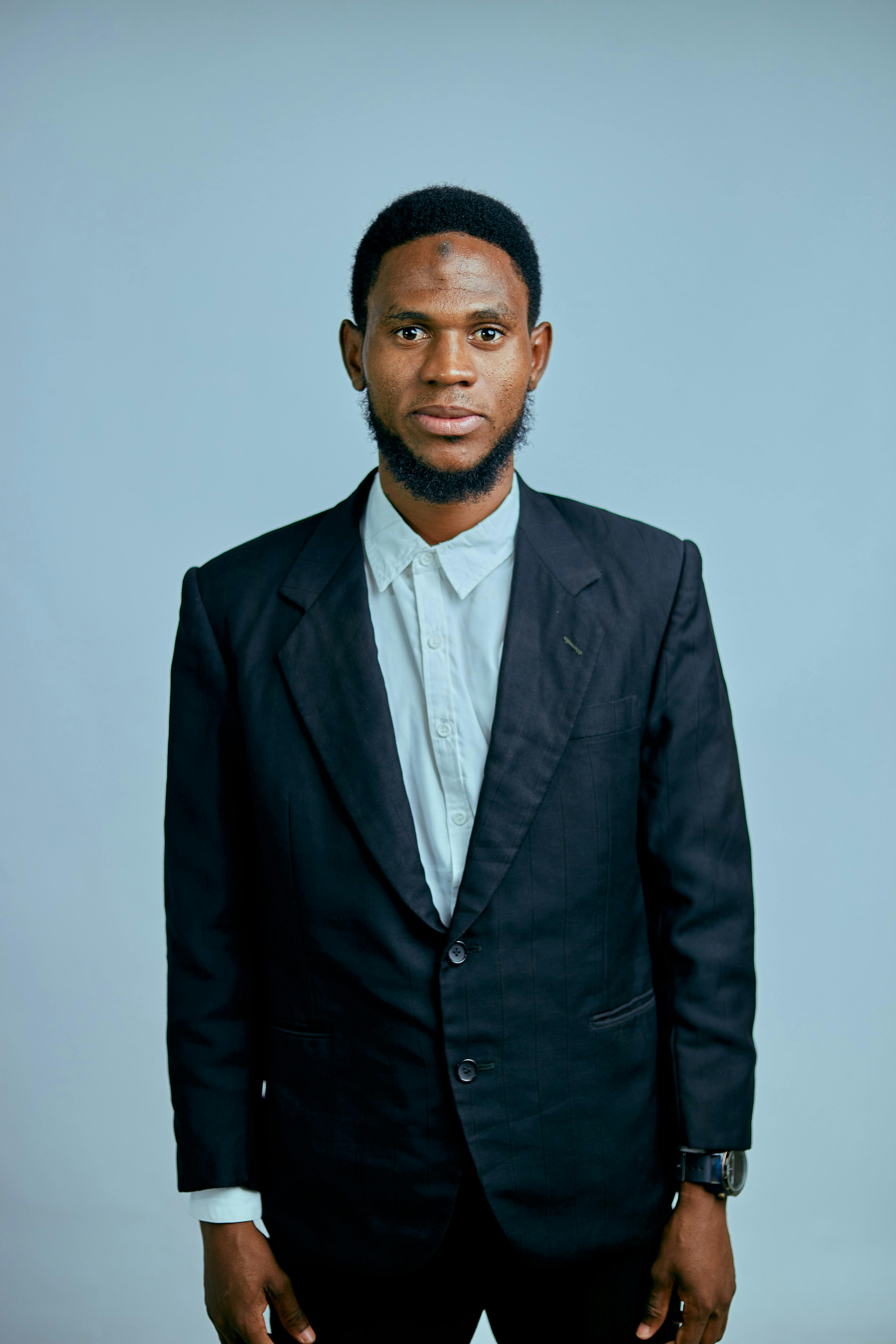 Studio portrait of a man in a formal black suit against a neutral background.