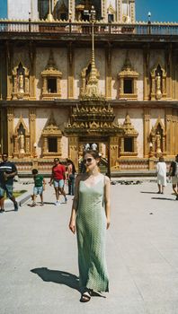 Woman in a green dress standing before Wat Chalong Temple in sunny Phuket.