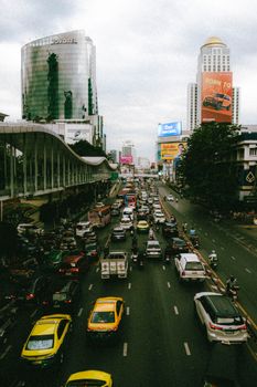 Vibrant street view in Bangkok showing busy traffic under cloudy skies.