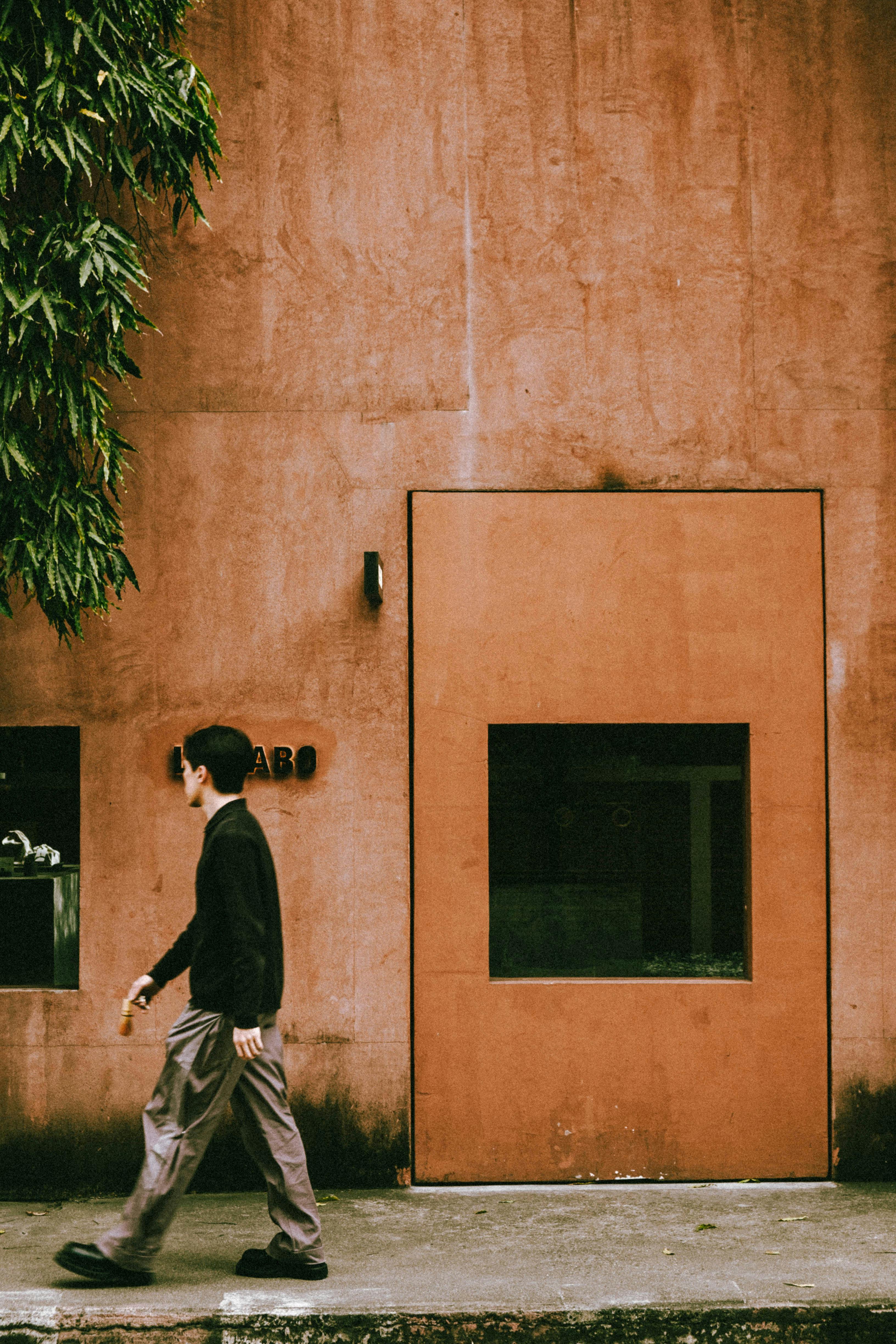 無料 バンコクにあるミニマリストなコーヒーショップの前を歩く男性。都会的なスタイルと温かい雰囲気が融合した空間です。 写真素材