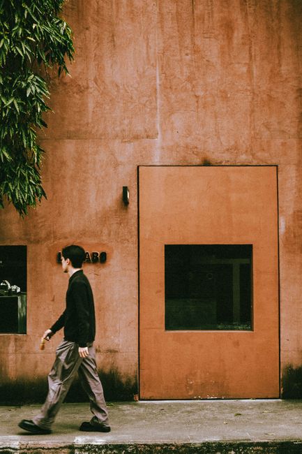 A man walks past a minimalist coffee shop facade in Bangkok, capturing a blend of urban style and warm ambiance.