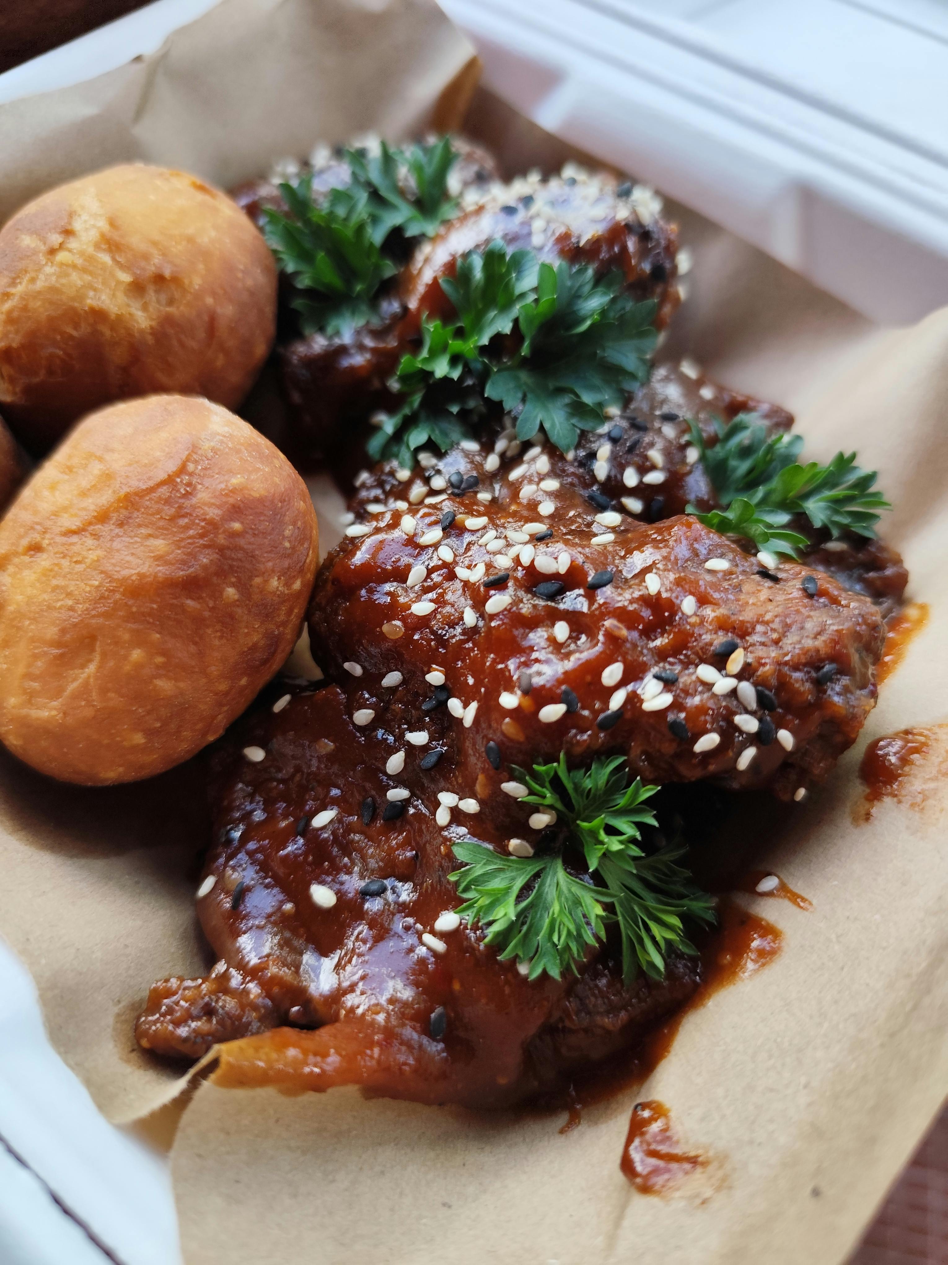 Golden brown chicken wings glazed with harissa honey sauce, garnished with fresh cilantro and sesame seeds on a white serving platter with lemon wedges
