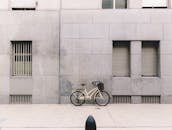 白天，自行车带着篮子停在人行道旁灰色混凝土建筑的墙壁上