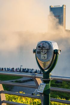 Coin operated viewer overlooking the misty Niagara Falls as tourists observe the iconic waterfall.