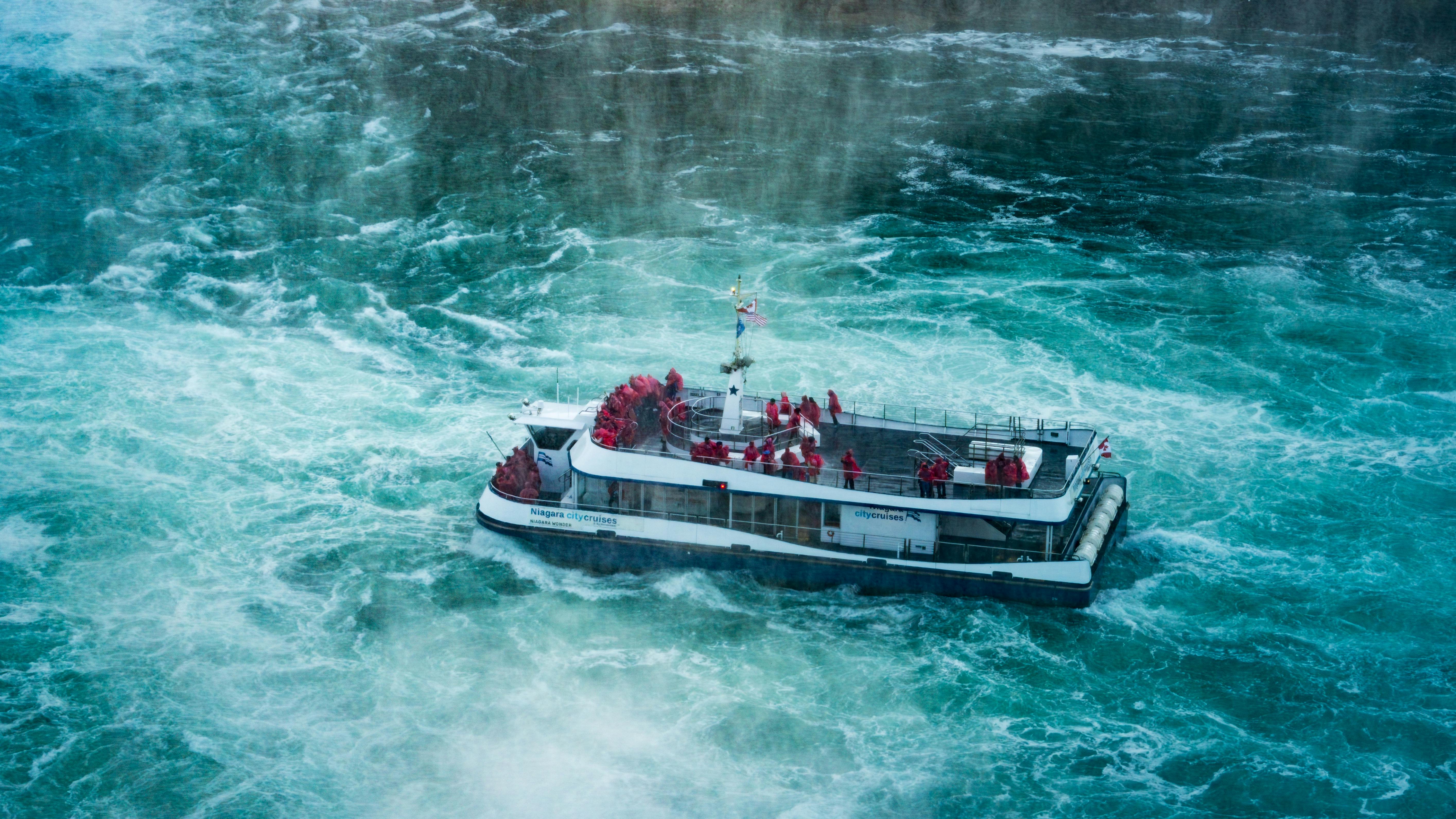 Tourists in red ponchos enjoy a boat tour at Niagara Falls in misty conditions.