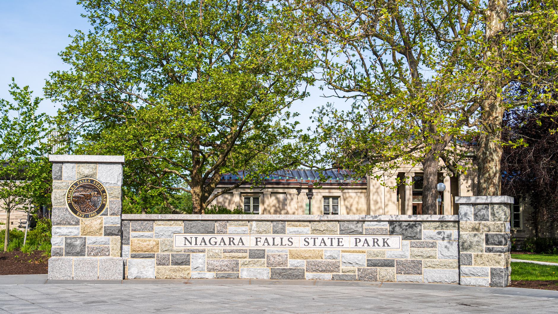 Stone wall signage of historic Niagara Falls State Park under a clear blue sky, perfect for tourists.