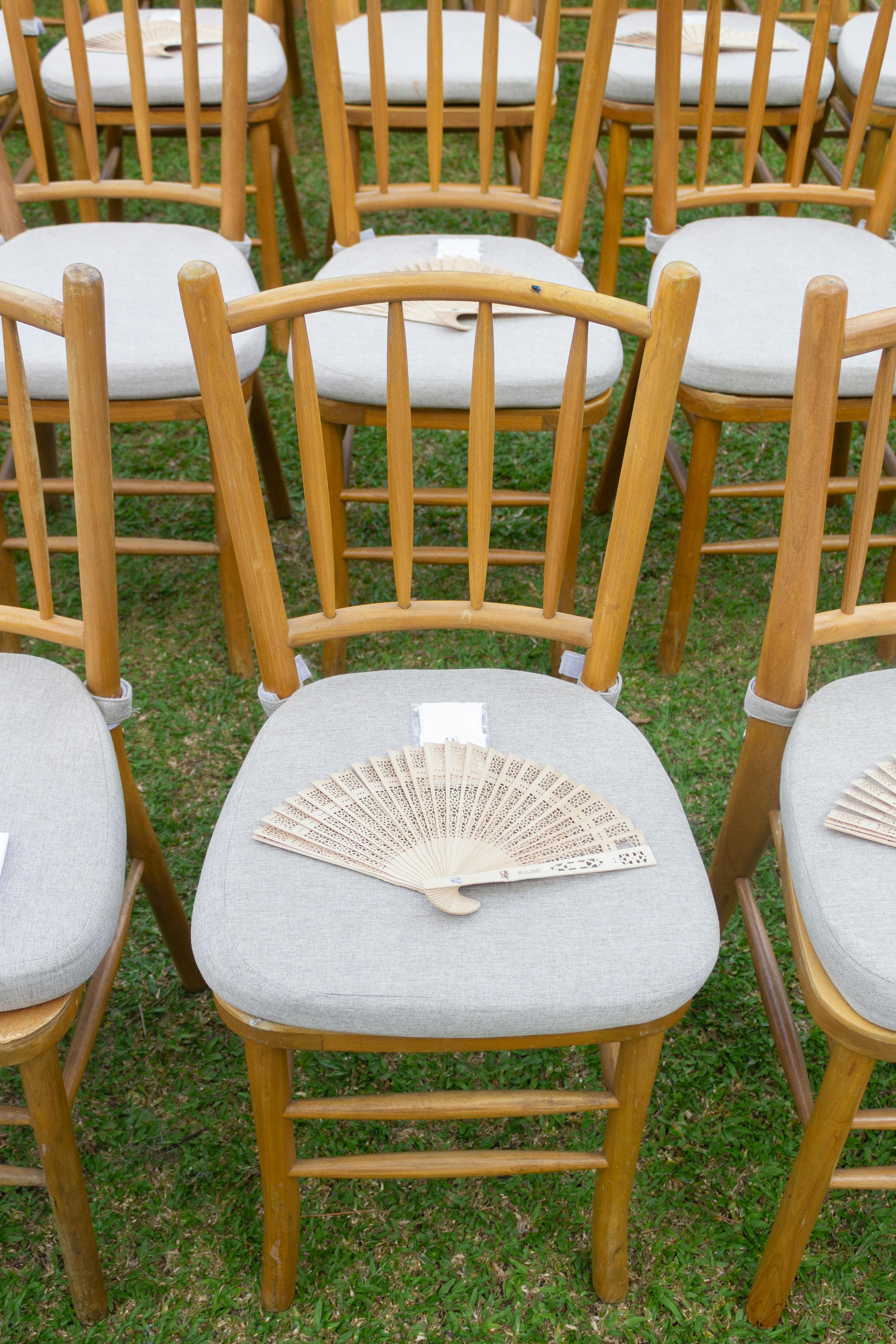 Elegant outdoor wedding setting with wooden chairs and decorative hand fans.