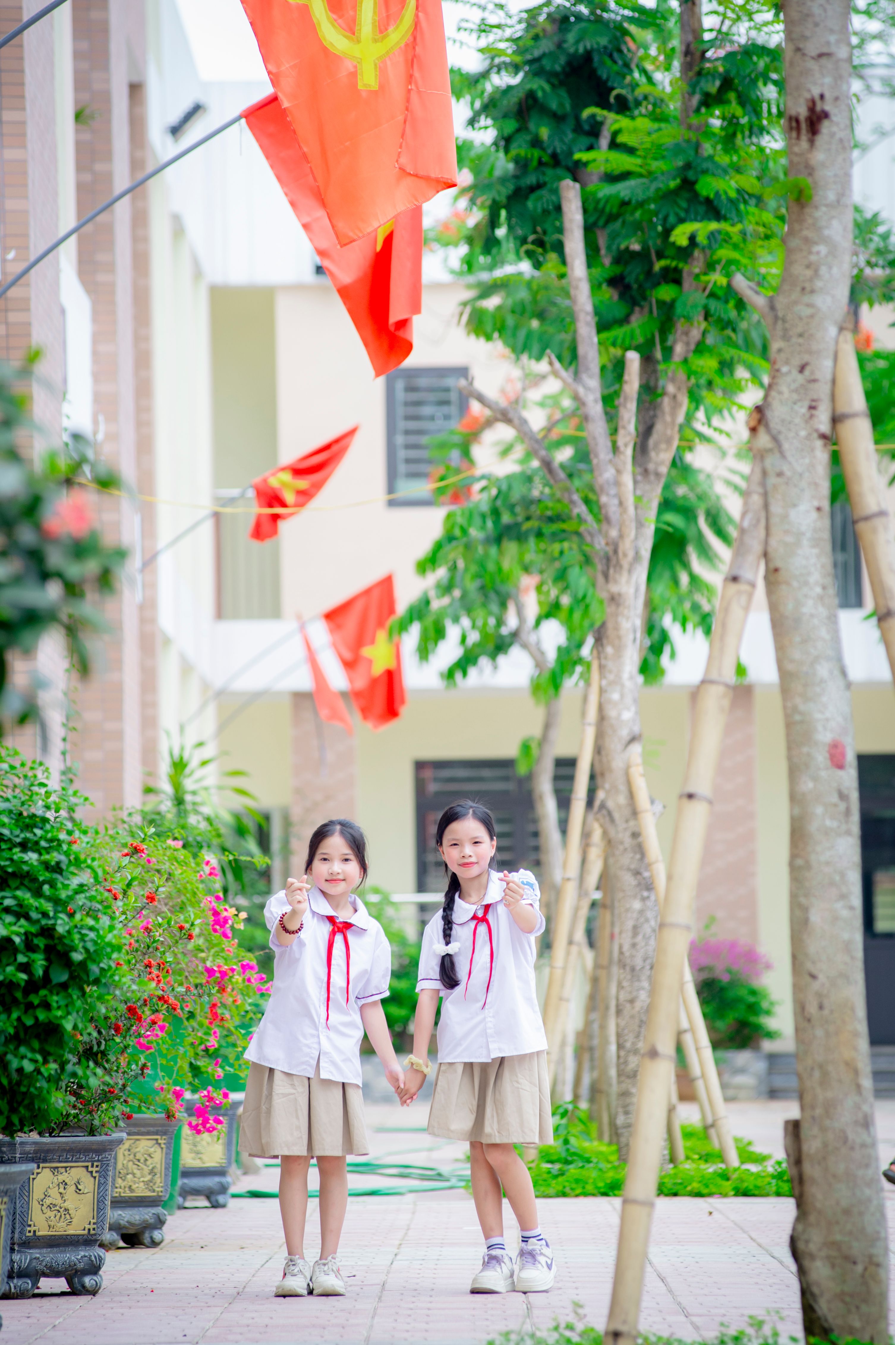 Two schoolgirls in uniforms standing outdoors under red flags in Hà Nội, Việt Nam.