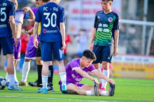 Teenage players engaged in a football match, showcasing teamwork and energy on a sunny day in Hanoi.