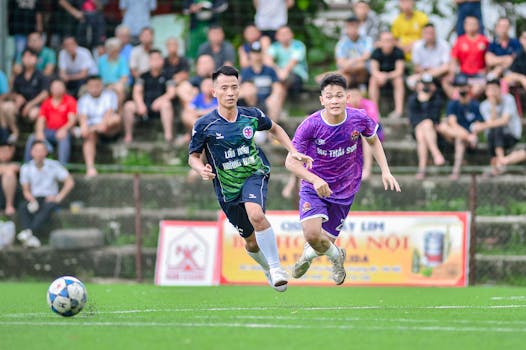 Two young athletes competing in a soccer match in Hà Nội with a vibrant crowd in the background.