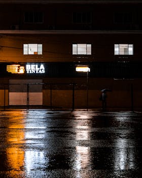 Moody urban scene with neon lights reflecting on wet pavement during a rainy night.