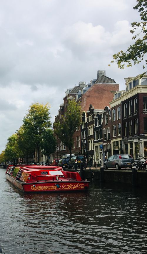 Free Charming canal view in Amsterdam featuring a vibrant tour boat and classic architecture. Stock Photo