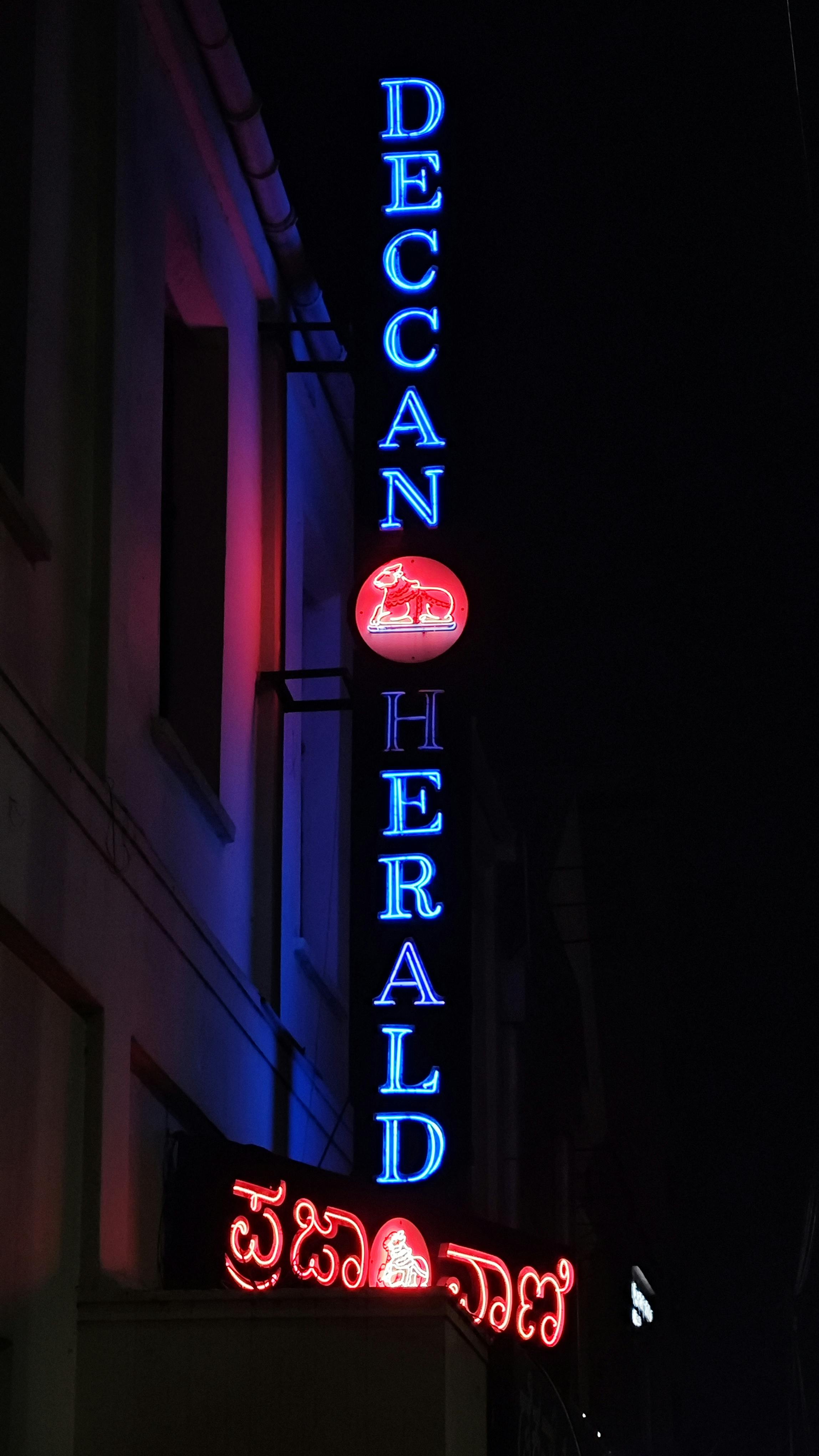 Kostnadsfria Vertikal neonskylt för Deccan Herald med text på engelska och regionala skrifter, som lyser på natten. Stock foto