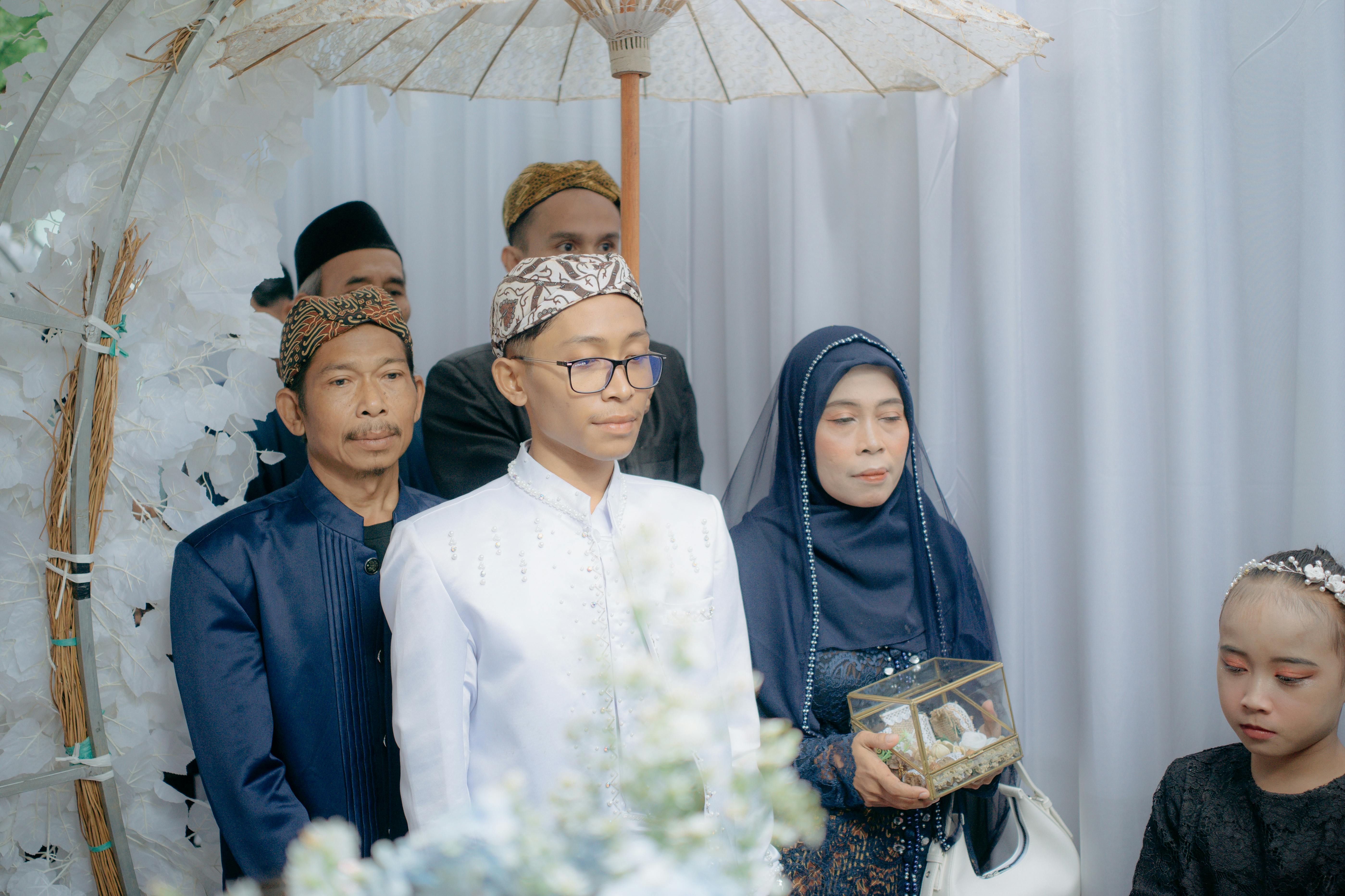 Family in traditional attire gathers for a ceremonial occasion under an ornate umbrella.