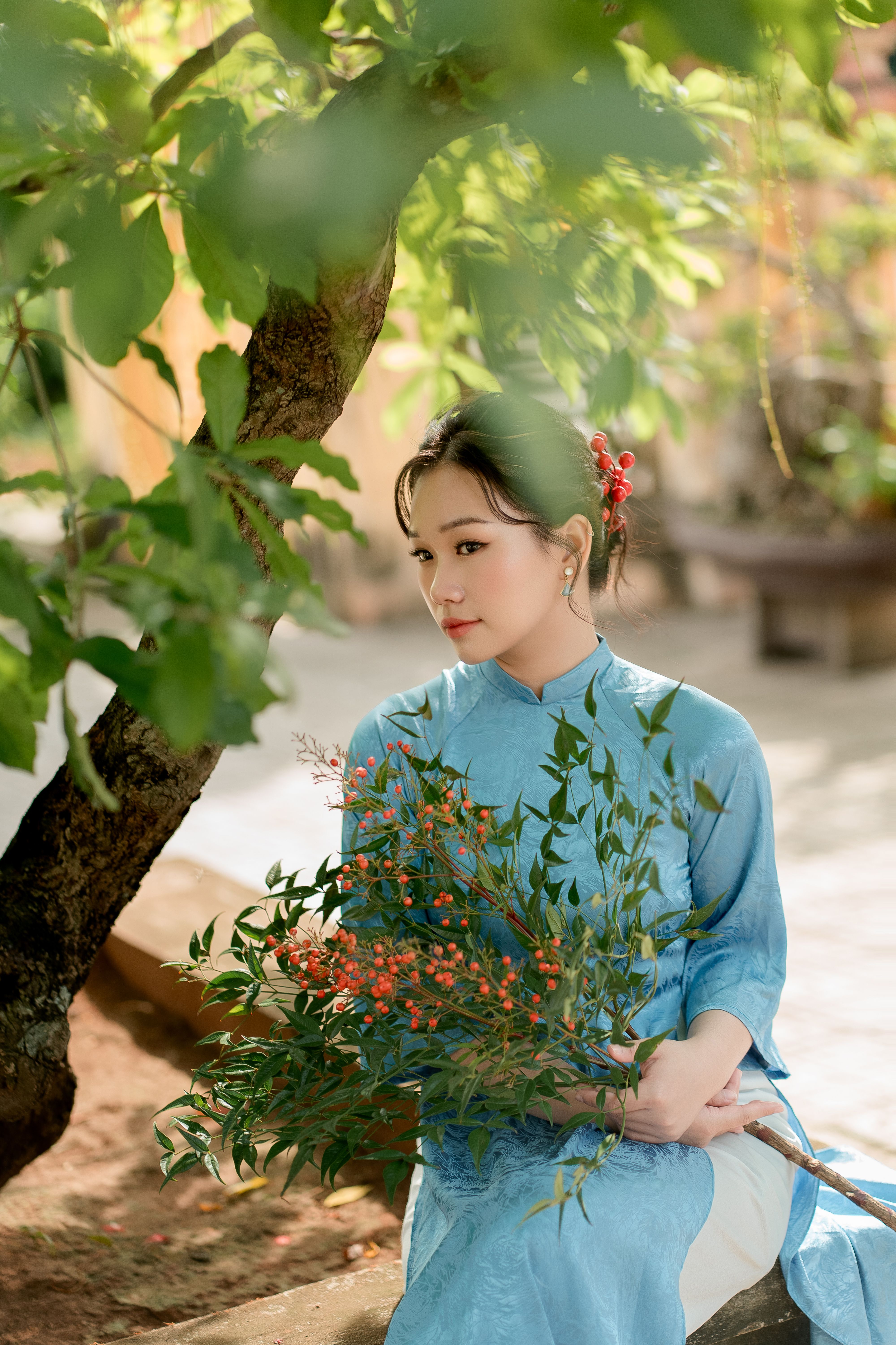 Elegant woman in blue traditional dress holding a bouquet in a sunlit garden.