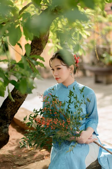 Elegant woman in blue traditional dress holding a bouquet in a sunlit garden.
