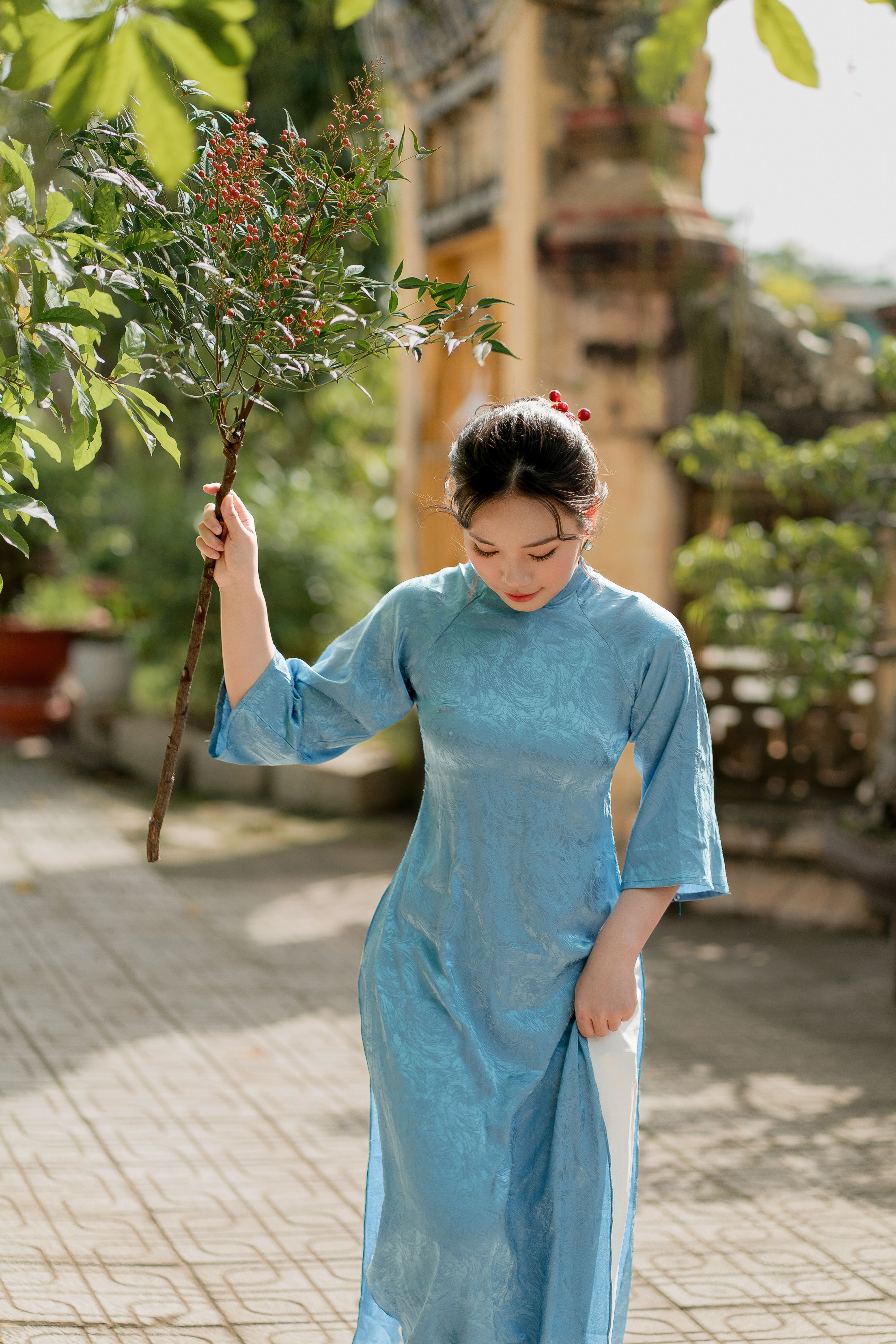 Woman in blue Vietnamese dress holding a branch, captured in an outdoor setting.
