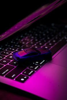 Stylish toy car on laptop keyboard with vibrant neon lighting, illustrating technology and miniatures.