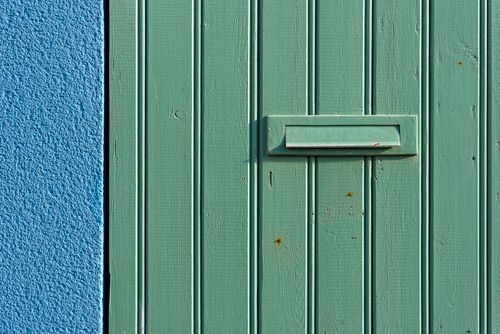Free A textured green wooden door with a mail slot against a vibrant blue wall, featuring a striking color contrast. Stock Photo