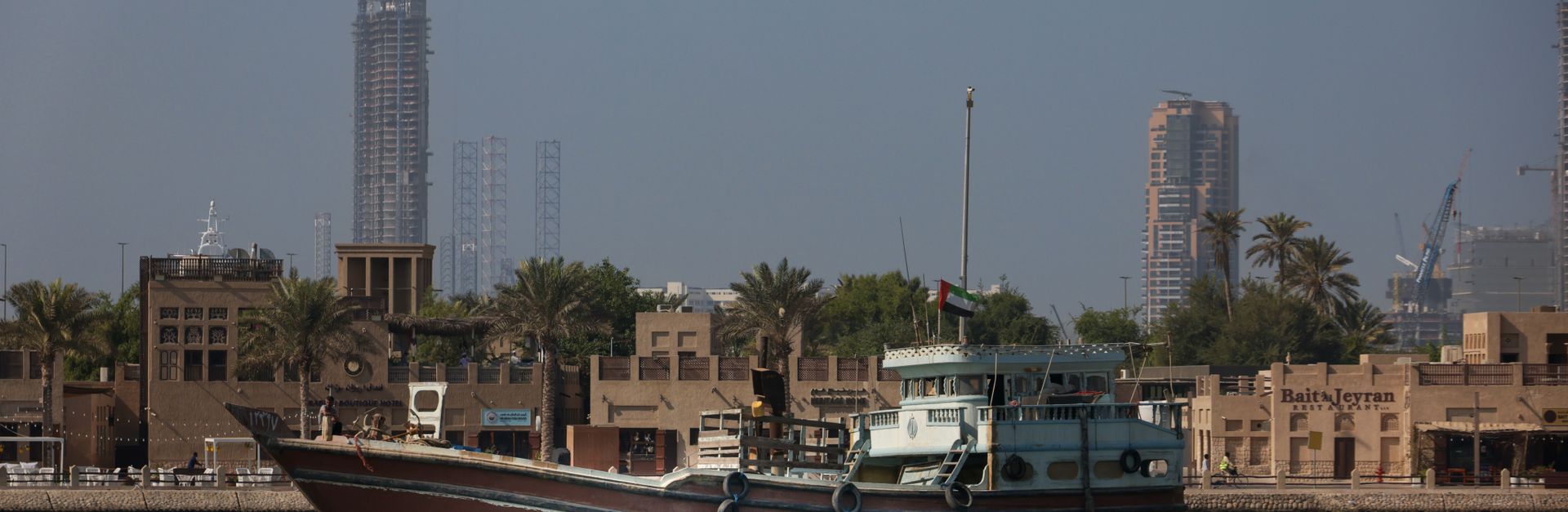 A traditional dhow sails peacefully on Dubai Creek with modern skyscrapers in the background.