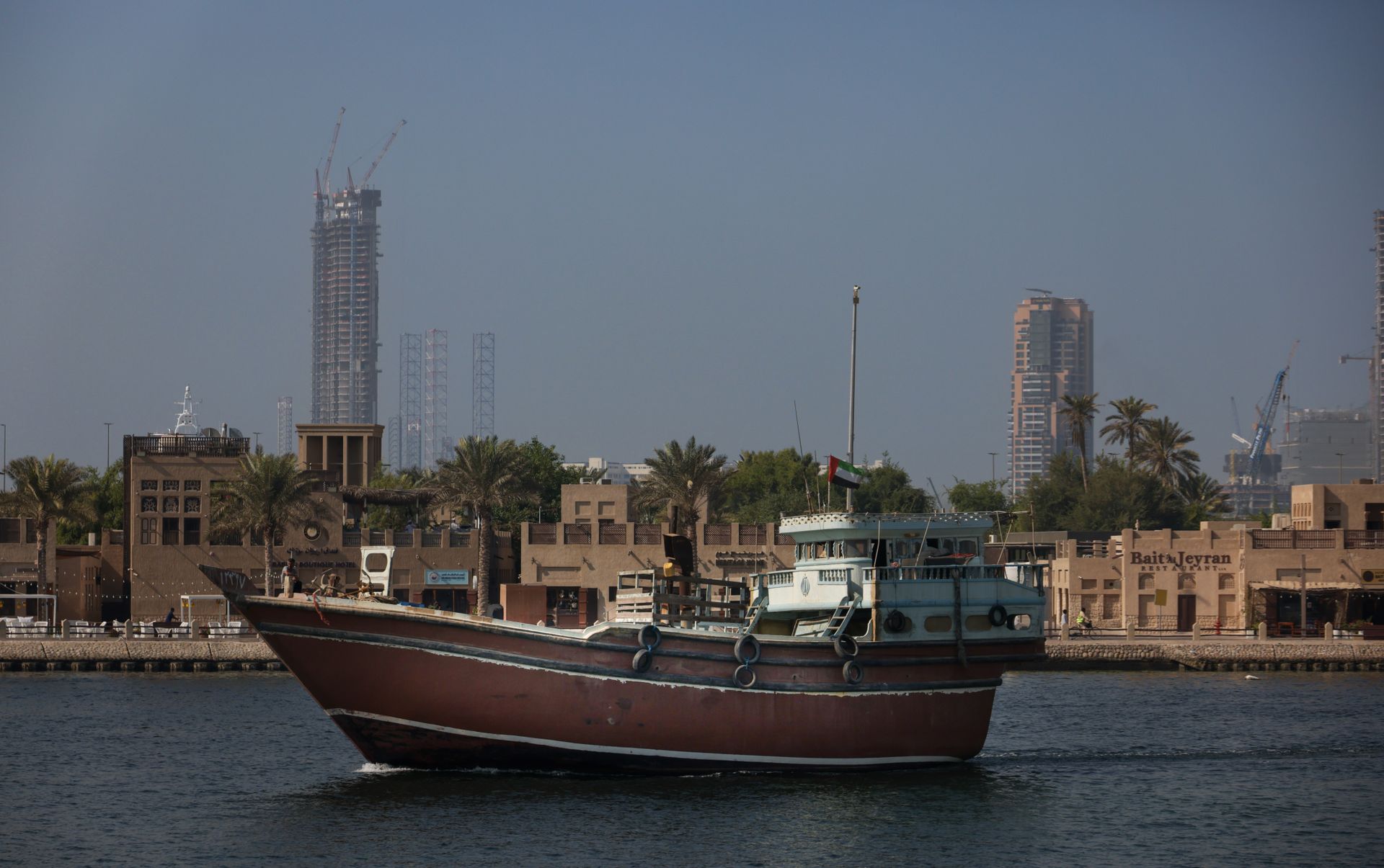 A traditional dhow sails peacefully on Dubai Creek with modern skyscrapers in the background.