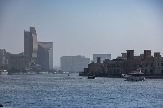 A serene view of modern and traditional buildings along a Dubai river with boats.