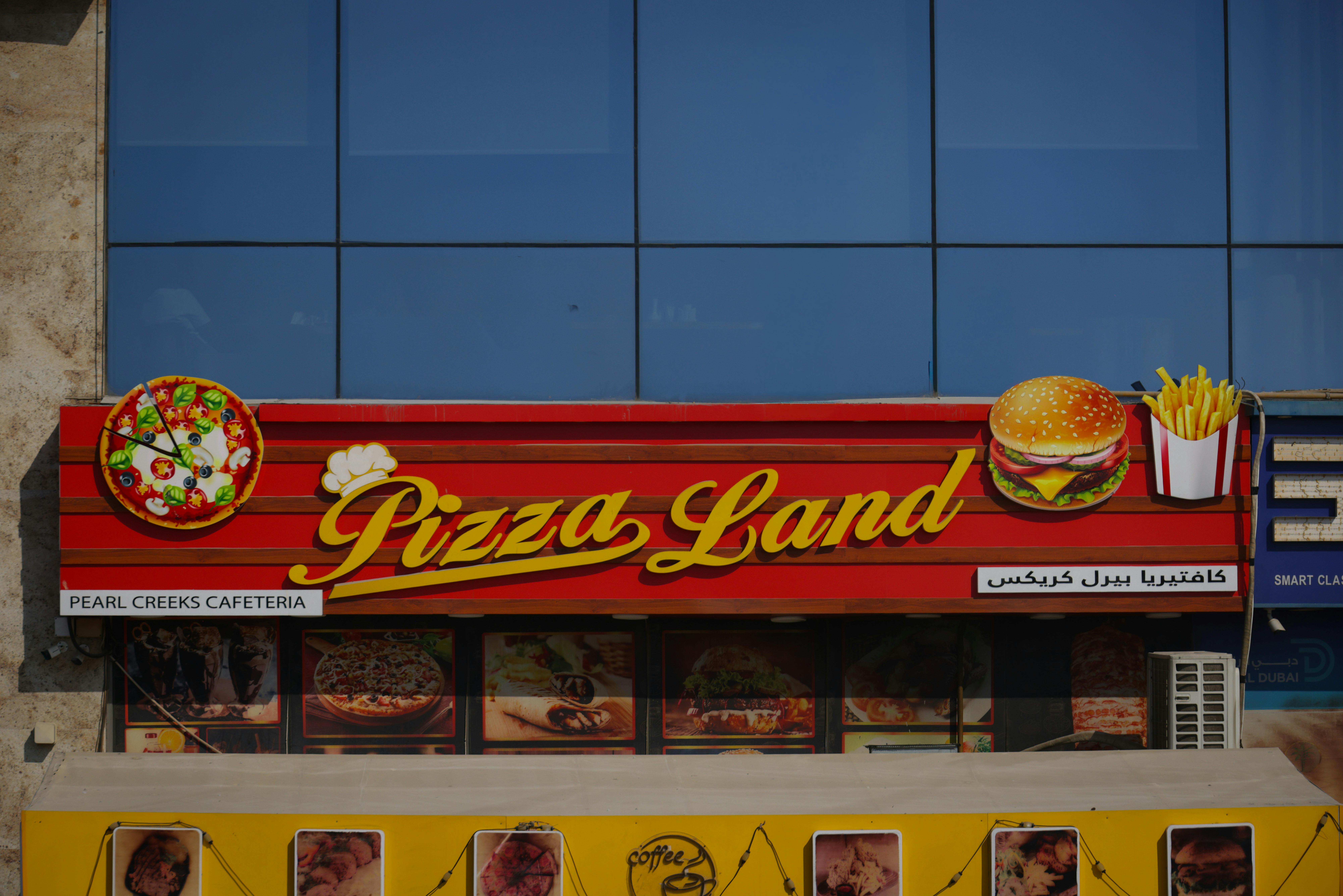 Bright sign for Pizza Land, showcasing pizza, burgers, and fries outside a modern building.