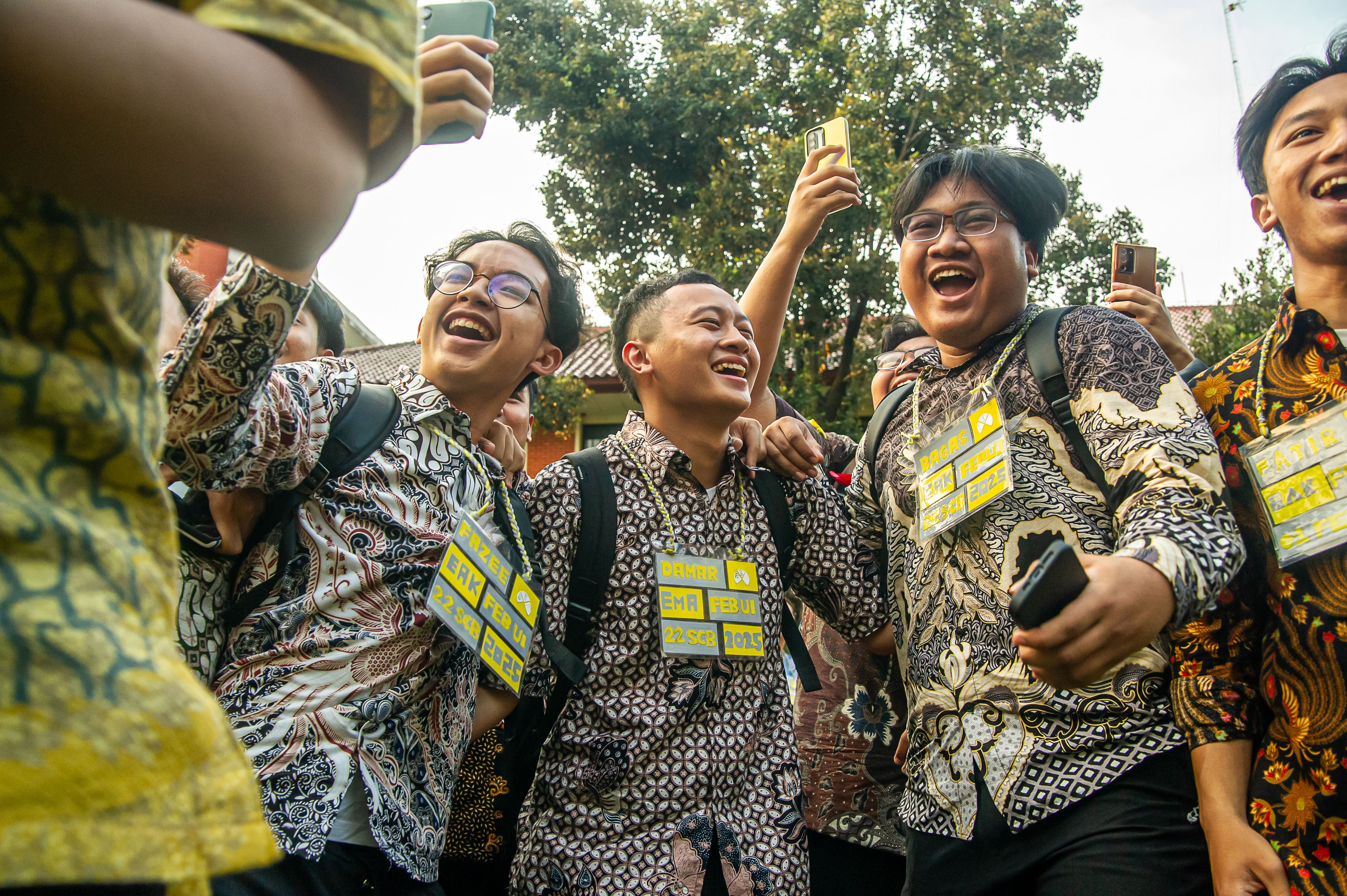A group of cheerful students in batik shirts celebrating together outdoors.