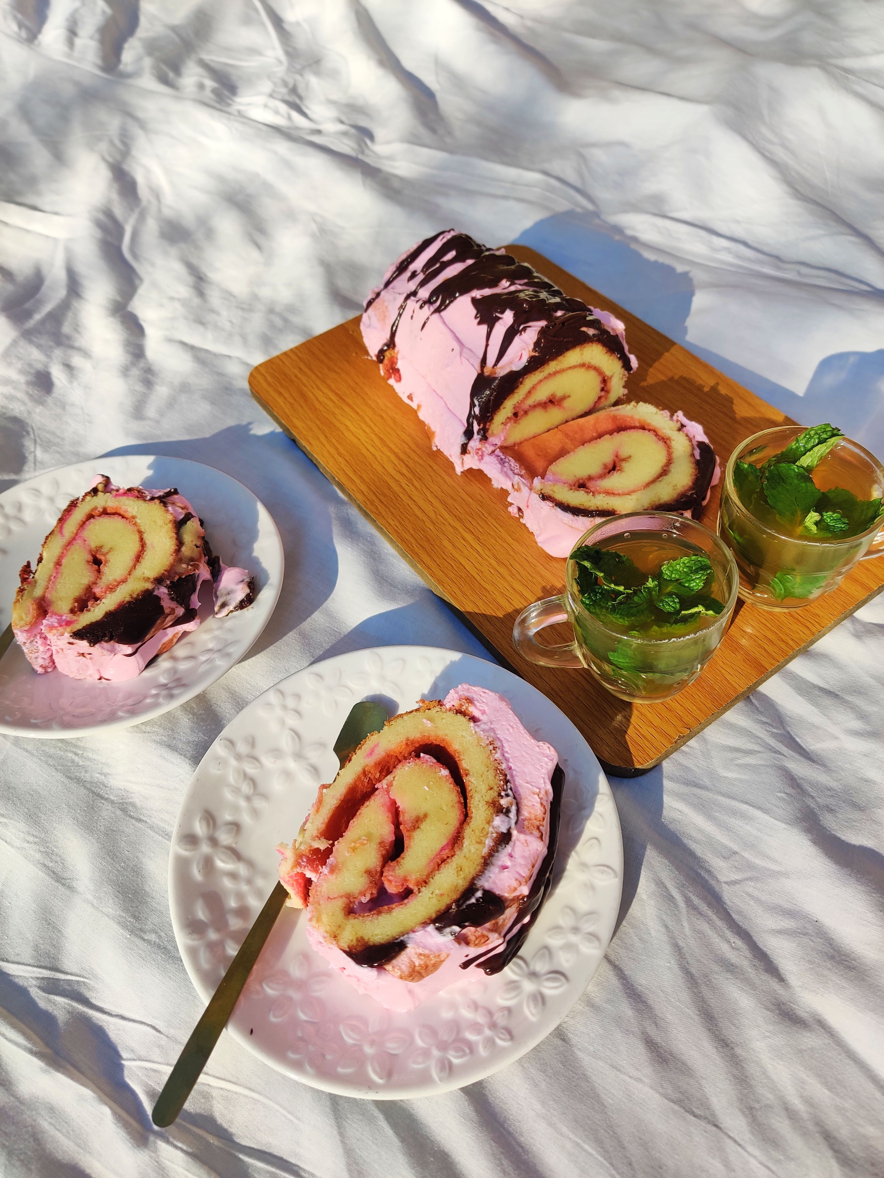 A sliced jelly roll cake showing a spiral of pale sponge and raspberry jam filling, dusted with powdered sugar on a wooden board.