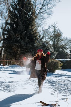 A woman joyously plays in the snow during a sunny winter day, showcasing a festive spirit.
