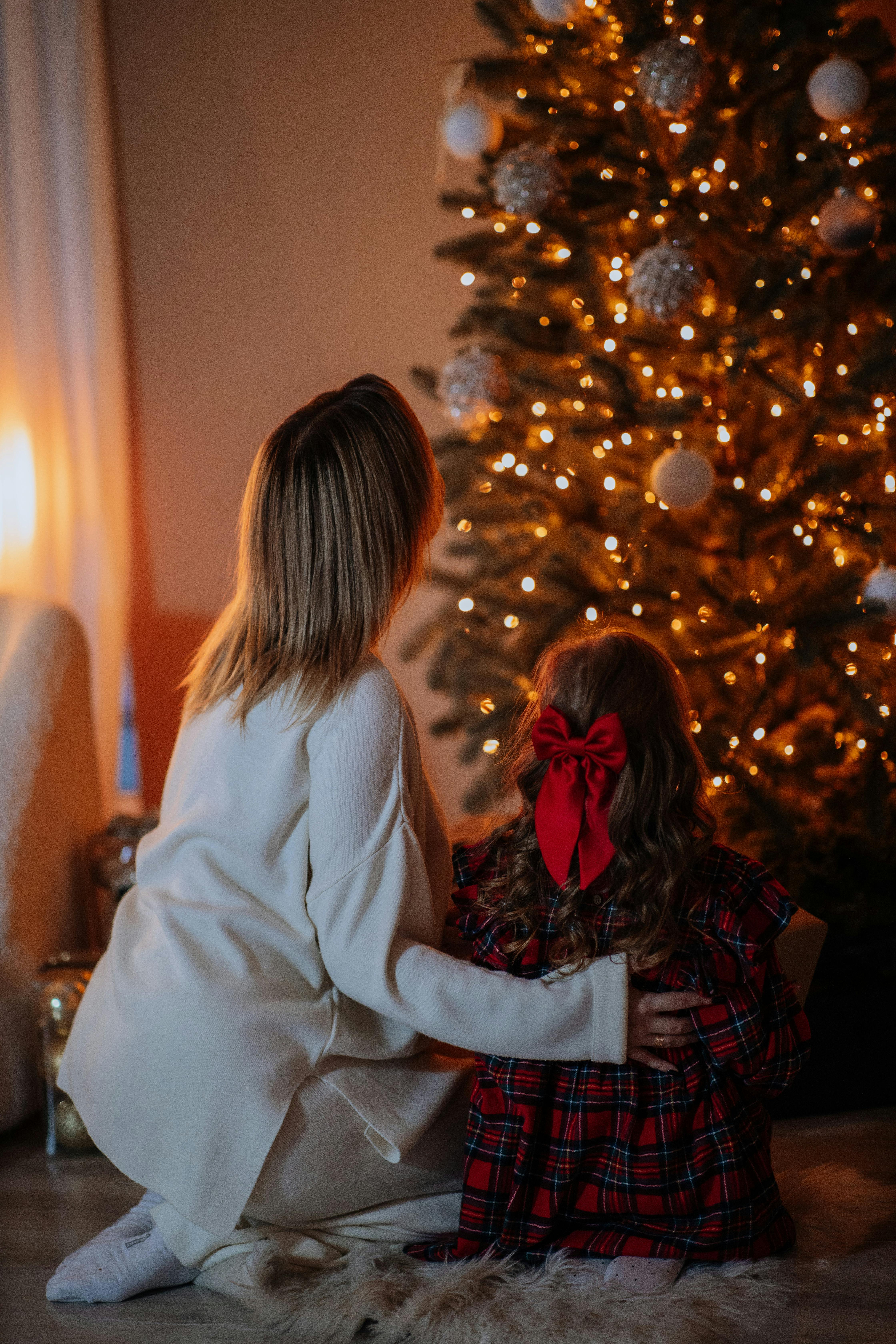 A warm moment as a mother and child admire a beautifully lit Christmas tree indoors.