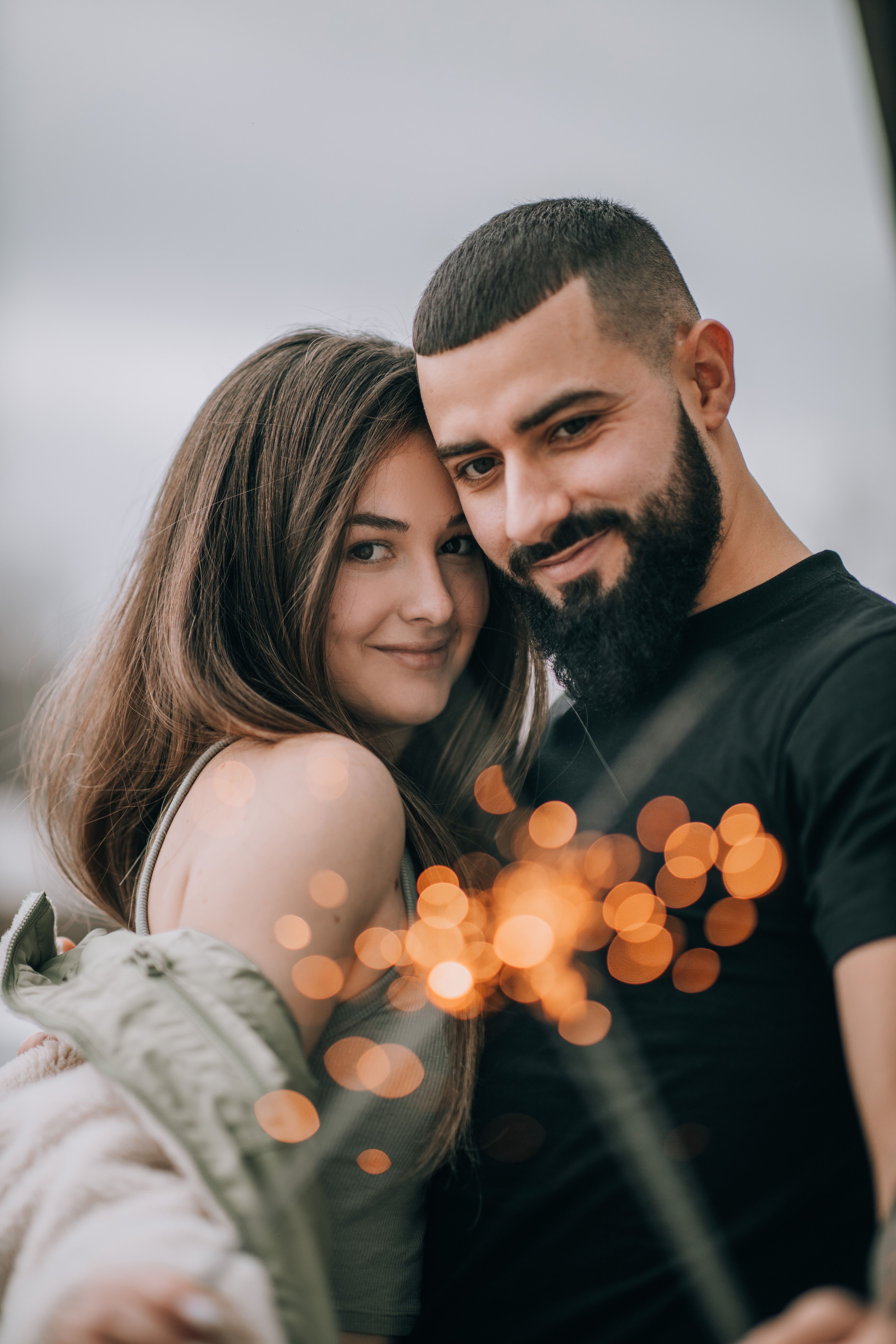 A smiling couple embraces and holds sparklers, creating a warm and festive atmosphere outdoors.