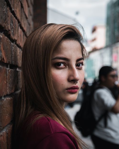 Free Close-up portrait of a woman with nose piercing leaning against a brick wall outdoors. Fashionable and intense look. Stock Photo