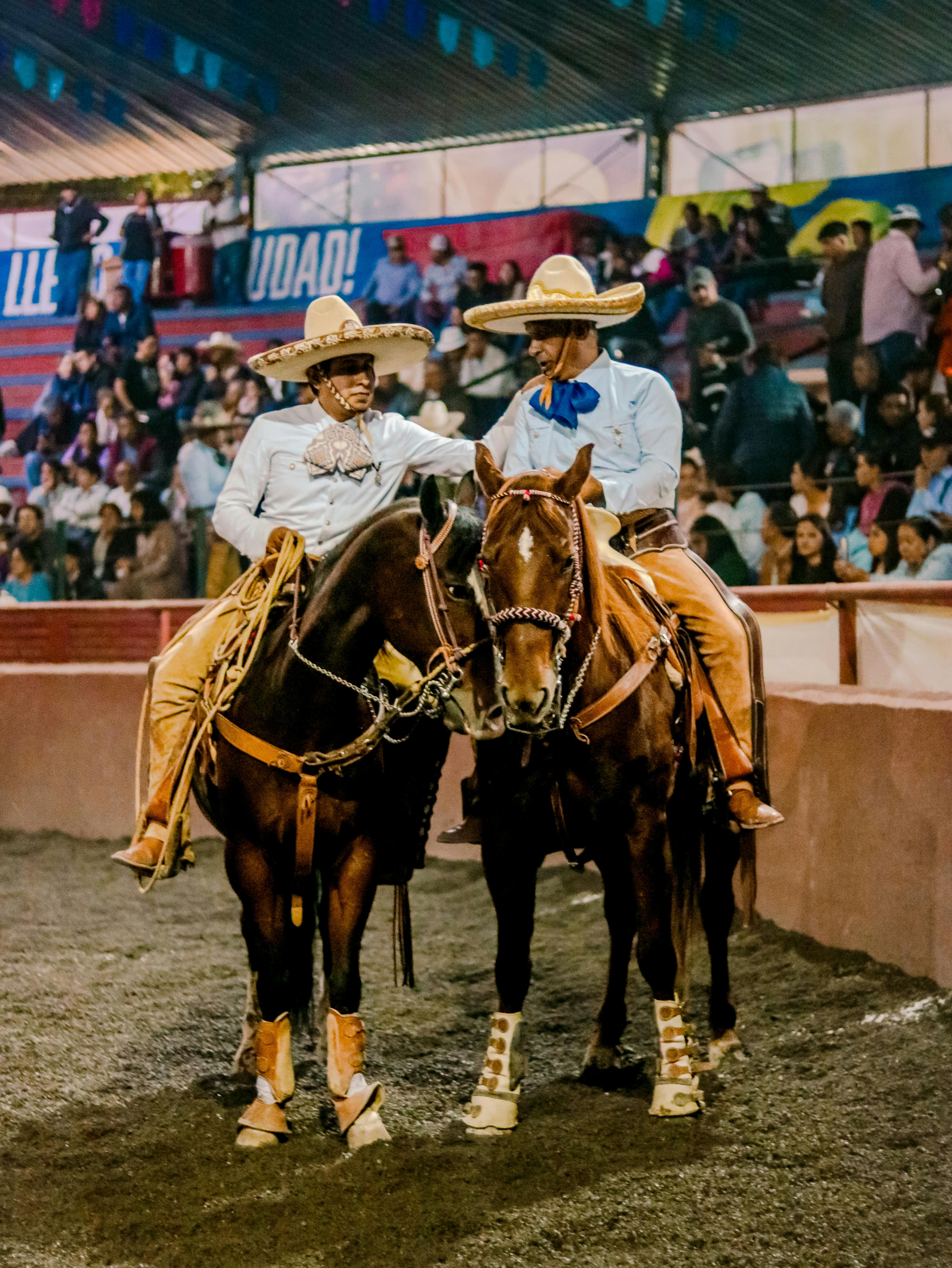 Two charros on horseback at a lively Mexican rodeo, showcasing traditional attire and equestrian skills.