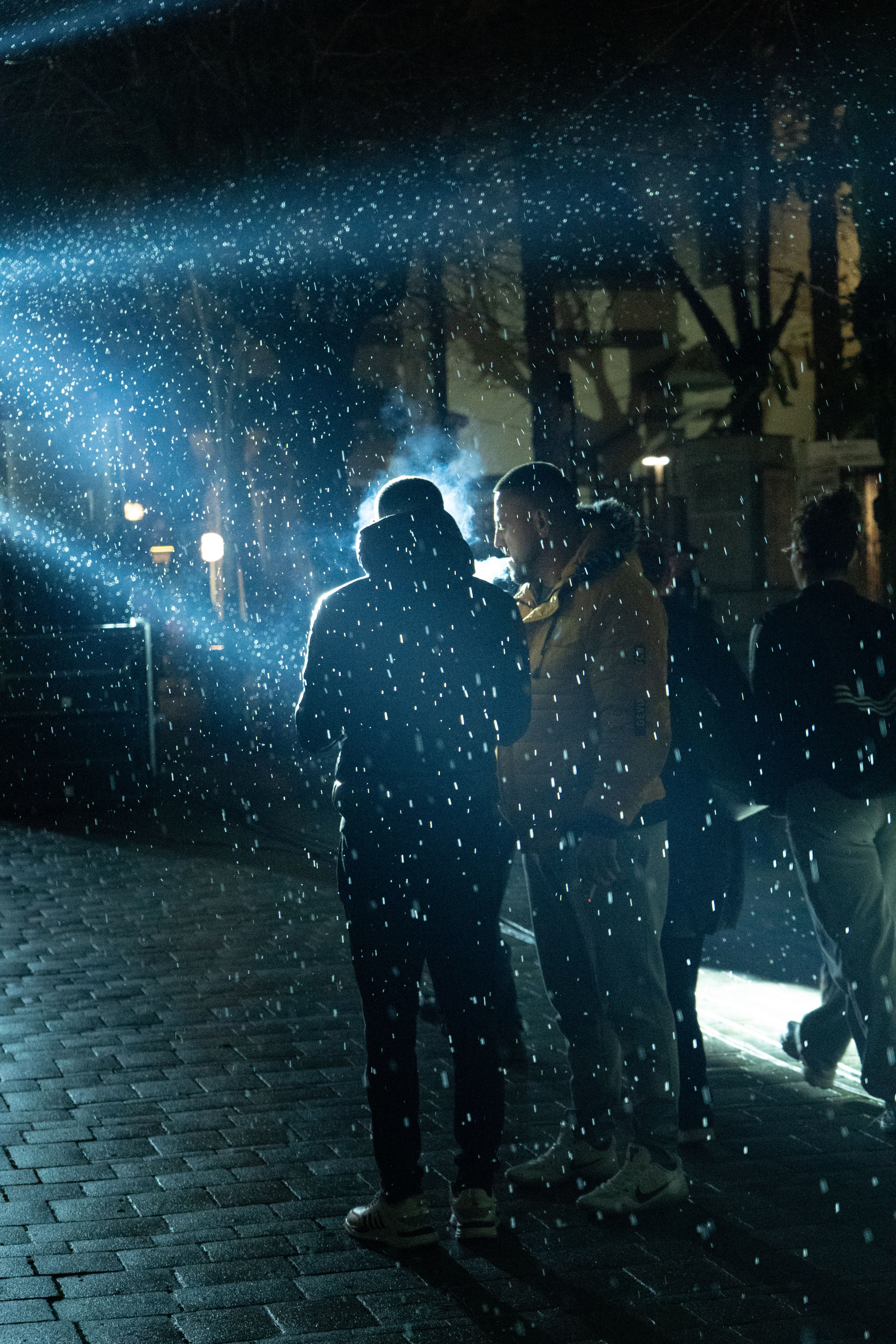 People walking under streetlights on a cobbled street as snow falls at night in Korçë, Albania