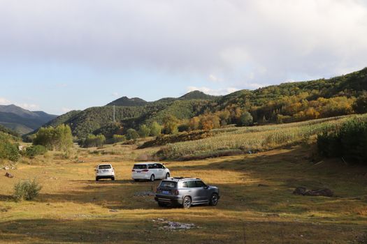 Explore the scenic valley landscape with off-road vehicles surrounded by lush hills and autumn foliage.