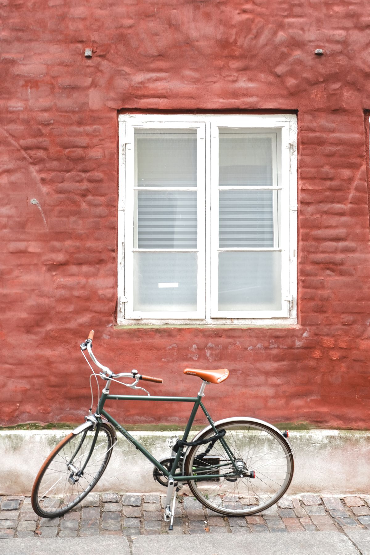 Unde te cazezi în Copenhaga - bicicletă verde sprijinită de un zid de cărămidă roșie