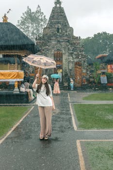 Young woman with umbrella in the rain at a historic Balinese temple. Cultural and serene atmosphere.