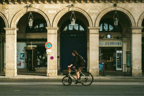 Free A cyclist riding past historic arches in Paris, showcasing urban life. Stock Photo
