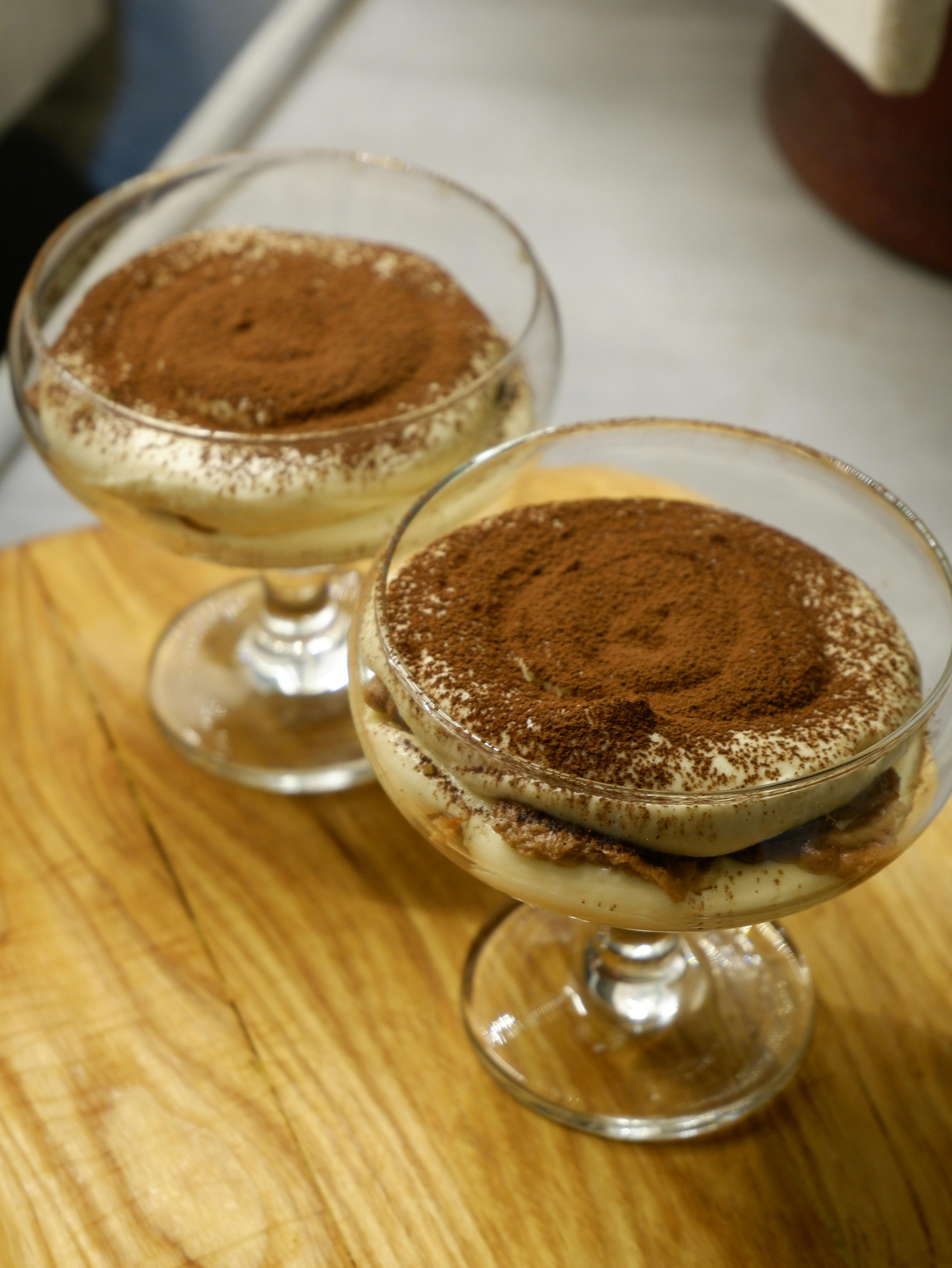 Tiramisu served in elegant glass cups, topped with cocoa powder on wood surface.