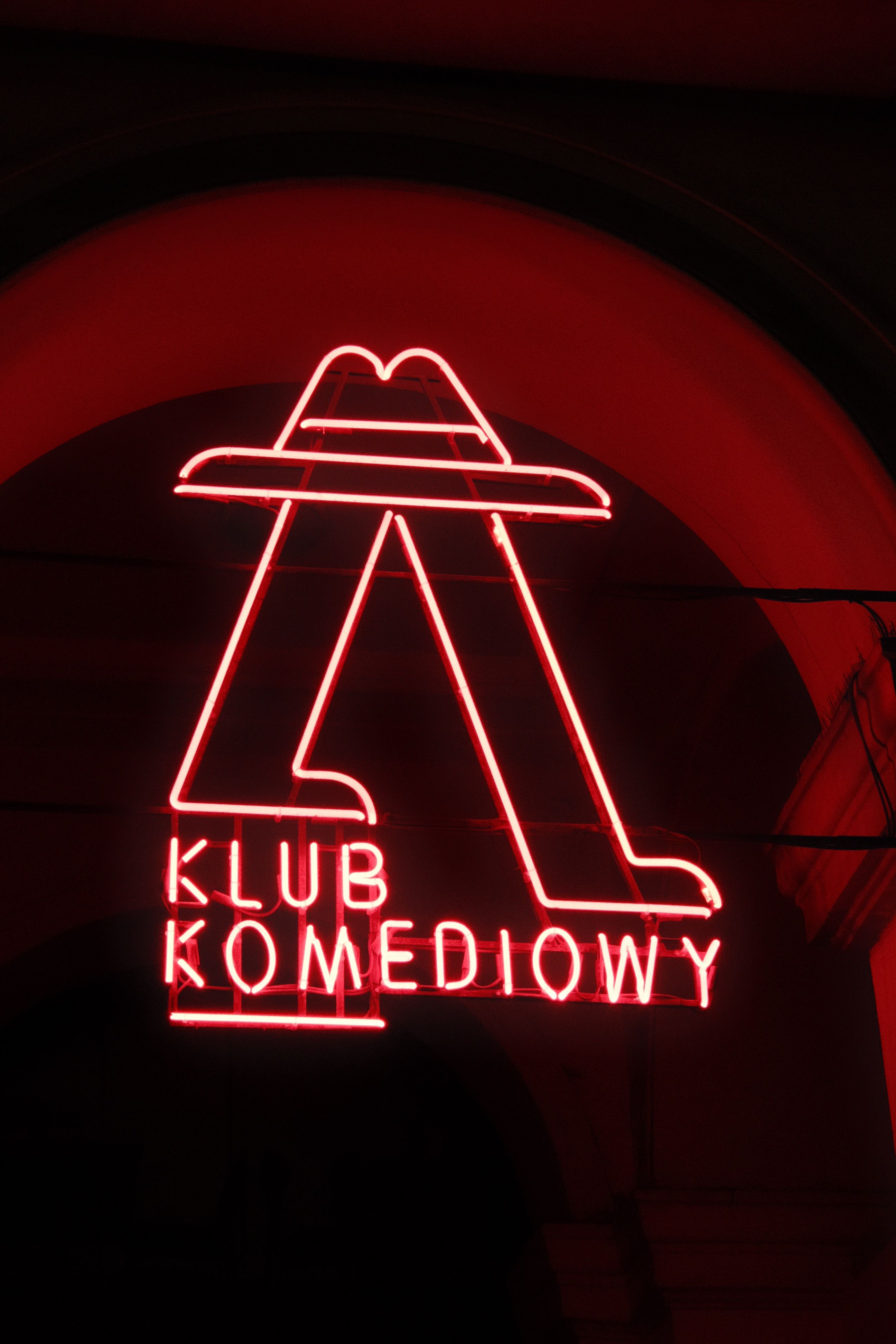 Bright red neon sign of Klub Komediowy glowing in the night, creating an urban aesthetic.